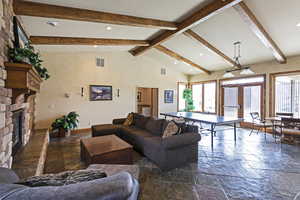 Living room featuring stone tile flooring, beam ceiling, a fireplace, recessed lighting, and high vaulted ceiling