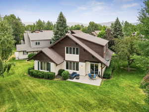 Rear view of property featuring a patio, a lawn, a shingled roof, and stucco siding