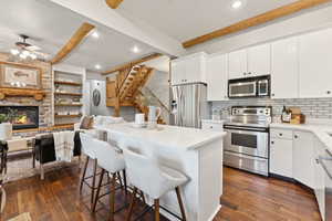 Kitchen with stainless steel appliances, a ceiling fan, open floor plan, a kitchen bar, and beamed ceiling