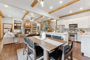 Dining area featuring a ceiling fan, beam ceiling, dark wood-style flooring, a stone fireplace, and recessed lighting