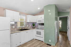 Kitchen featuring white appliances, vaulted ceiling, light wood finished floors, tasteful backsplash, and white cabinets