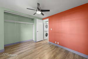 Laundry area with stacked washer / drying machine, wood finished floors, and a ceiling fan