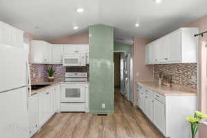 Kitchen with white appliances, lofted ceiling, white cabinetry, light wood-type flooring, and decorative backsplash
