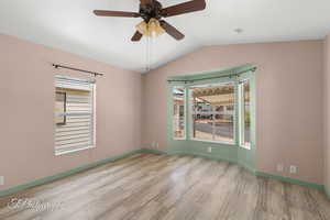Unfurnished room featuring wood finished floors, lofted ceiling, ceiling fan, and a smoke detector