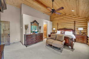 Bedroom featuring wood ceiling, rustic walls, carpet, high vaulted ceiling, and connected bathroom