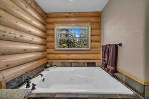 Bathroom featuring a tub with jets and rustic walls