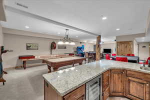 Kitchen featuring beverage cooler, brown cabinetry, open floor plan, light stone countertops, and recessed lighting