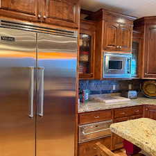 Kitchen with built in appliances, a warming drawer, tasteful backsplash, and light stone counters