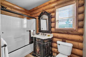 Full bathroom featuring log walls, vanity, and bath / shower combo with glass door