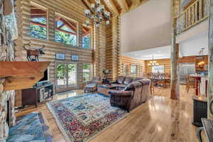 Living area featuring a chandelier, rustic walls, high vaulted ceiling, light wood-type flooring, and plenty of natural light
