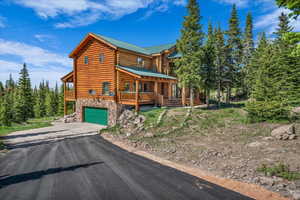 Log cabin featuring log exterior, stone siding, asphalt driveway, an attached garage, and a metal roof