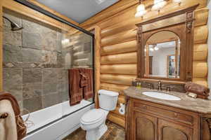 Full bath featuring rustic walls, vanity, combined bath / shower with glass door, ceiling fan, and stone finish flooring