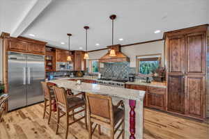 Kitchen with built in appliances, island exhaust hood, healthy amount of natural light, decorative backsplash, and ornamental molding