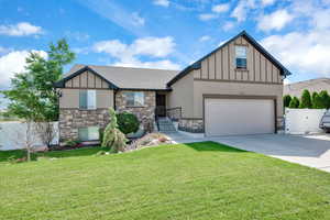 Tudor home featuring stone siding, driveway, board and batten siding, a gate, and a garage