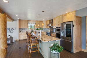 Kitchen featuring appliances with stainless steel finishes, wall chimney exhaust hood, light brown cabinets, dark wood finished floors, and recessed lighting