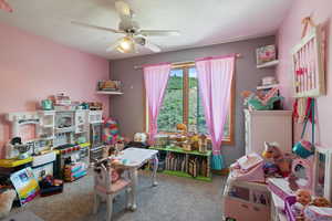 Rec room with carpet floors, ceiling fan, and a textured ceiling