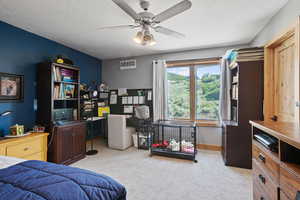 Bedroom with light carpet, a textured ceiling, an office area, and ceiling fan
