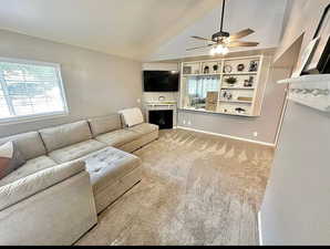 Living area featuring a ceiling fan, vaulted ceiling, a fireplace, and carpet floors