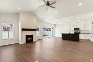 Unfurnished living room featuring vaulted ceiling, ceiling fan, light wood-style flooring, recessed lighting, and a lit fireplace