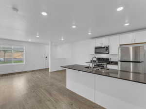 Kitchen with appliances with stainless steel finishes, dark countertops, light wood-type flooring, white cabinets, and recessed lighting