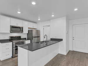 Kitchen with stainless steel appliances, dark countertops, light wood finished floors, white cabinets, and a peninsula