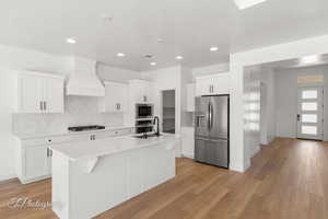 Kitchen with appliances with stainless steel finishes, an island with sink, light countertops, decorative backsplash, and white cabinets