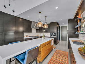 Kitchen featuring modern cabinets, hanging light fixtures, a breakfast bar, a kitchen island, and light stone counters