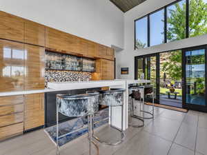 Kitchen featuring brown cabinetry, tasteful backsplash, modern cabinets, a high ceiling, and light tile patterned flooring