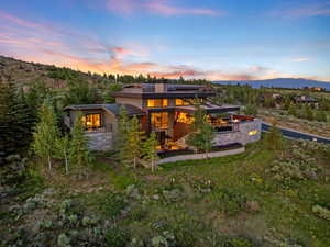 Back of house at dusk with roof mounted solar panels, a chimney, a mountain view, a patio, and stone siding