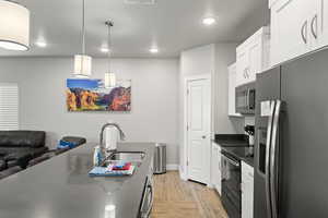 Kitchen with stainless steel appliances, dark countertops, light wood-style floors, white cabinets, and recessed lighting
