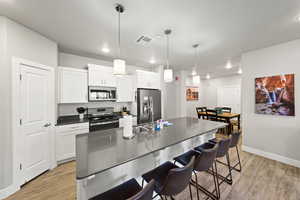 Kitchen featuring stainless steel appliances, light wood-type flooring, dark countertops, a breakfast bar area, and white cabinetry