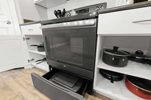 Kitchen view of light wood-style floors, white cabinets, and electric stove