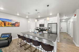 Kitchen with appliances with stainless steel finishes, dark countertops, a breakfast bar area, light wood-type flooring, and recessed lighting