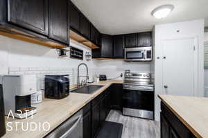Kitchen featuring appliances with stainless steel finishes, butcher block countertops, light wood-style flooring, and dark cabinetry