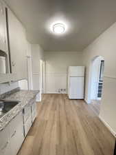 Kitchen with arched walkways, freestanding refrigerator, light wood finished floors, and white cabinetry