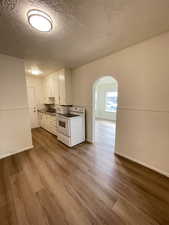 Kitchen featuring arched walkways, a textured ceiling, white appliances, white cabinetry, and light wood finished floors