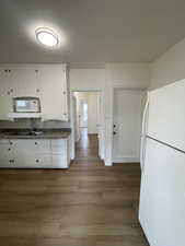 Kitchen with white appliances, white cabinetry, and dark wood-style floors