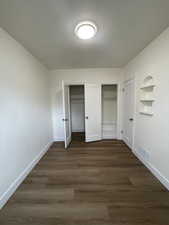 Unfurnished bedroom with multiple closets and dark wood-style floors