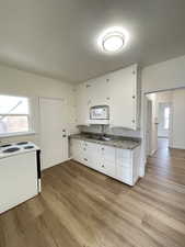 Kitchen with white appliances, white cabinetry, and light wood-type flooring