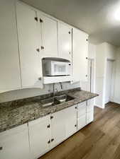 Kitchen with dark wood-style floors, white cabinets, dark countertops, and white microwave