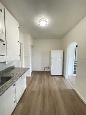 Kitchen featuring arched walkways, white cabinetry, light wood-style floors, white appliances, and dark countertops