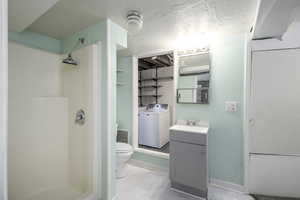 Bathroom featuring washer / dryer, a stall shower, marble look tiles, and vanity