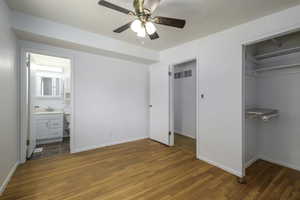 Unfurnished bedroom featuring wood finished floors, a closet, ensuite bath, and ceiling fan