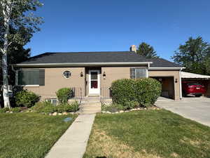 View of front of property featuring a front yard, driveway, an attached garage, a chimney, and brick siding