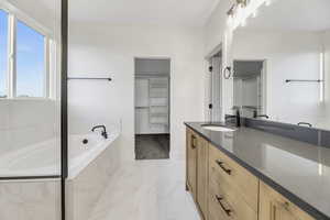 Full bathroom featuring double vanity, a garden tub, a walk in closet, and light marble finish flooring