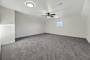 Empty room featuring vaulted ceiling, dark colored carpet, and ceiling fan