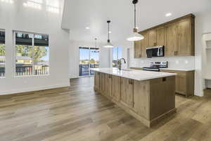 Kitchen featuring brown cabinets, backsplash, pendant lighting, stainless steel appliances, and a center island with sink
