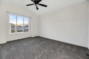 Empty room featuring lofted ceiling, dark colored carpet, and a ceiling fan