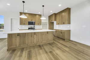 Kitchen with decorative backsplash, pendant lighting, a center island with sink, light wood-type flooring, and appliances with stainless steel finishes