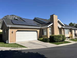 Single story home featuring a garage, brick siding, concrete driveway, and solar panels